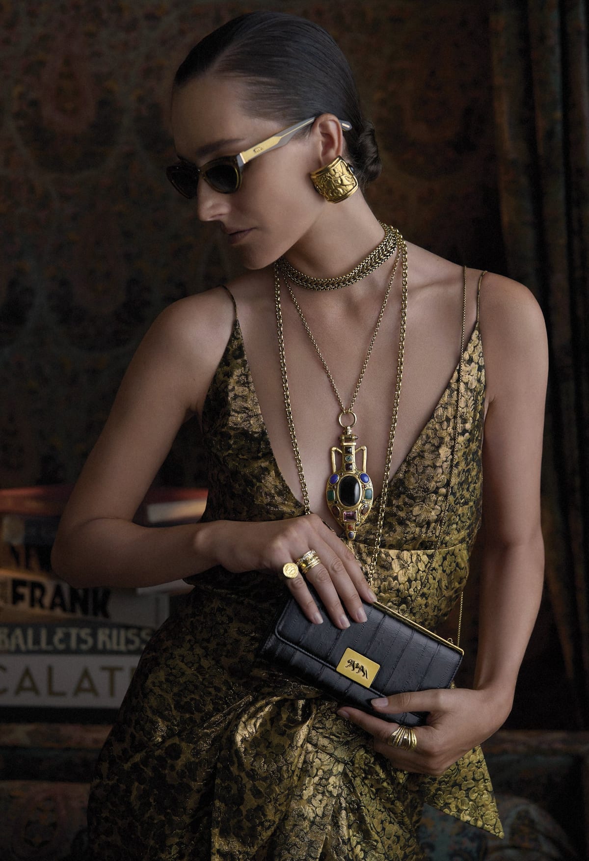 A model in a gold brocade dress wearing the Pantokrator Pendant Necklace and a wide gold cuff, holding a black clutch, from the Sabyasachi x Met Byzantine jewelry collaboration
